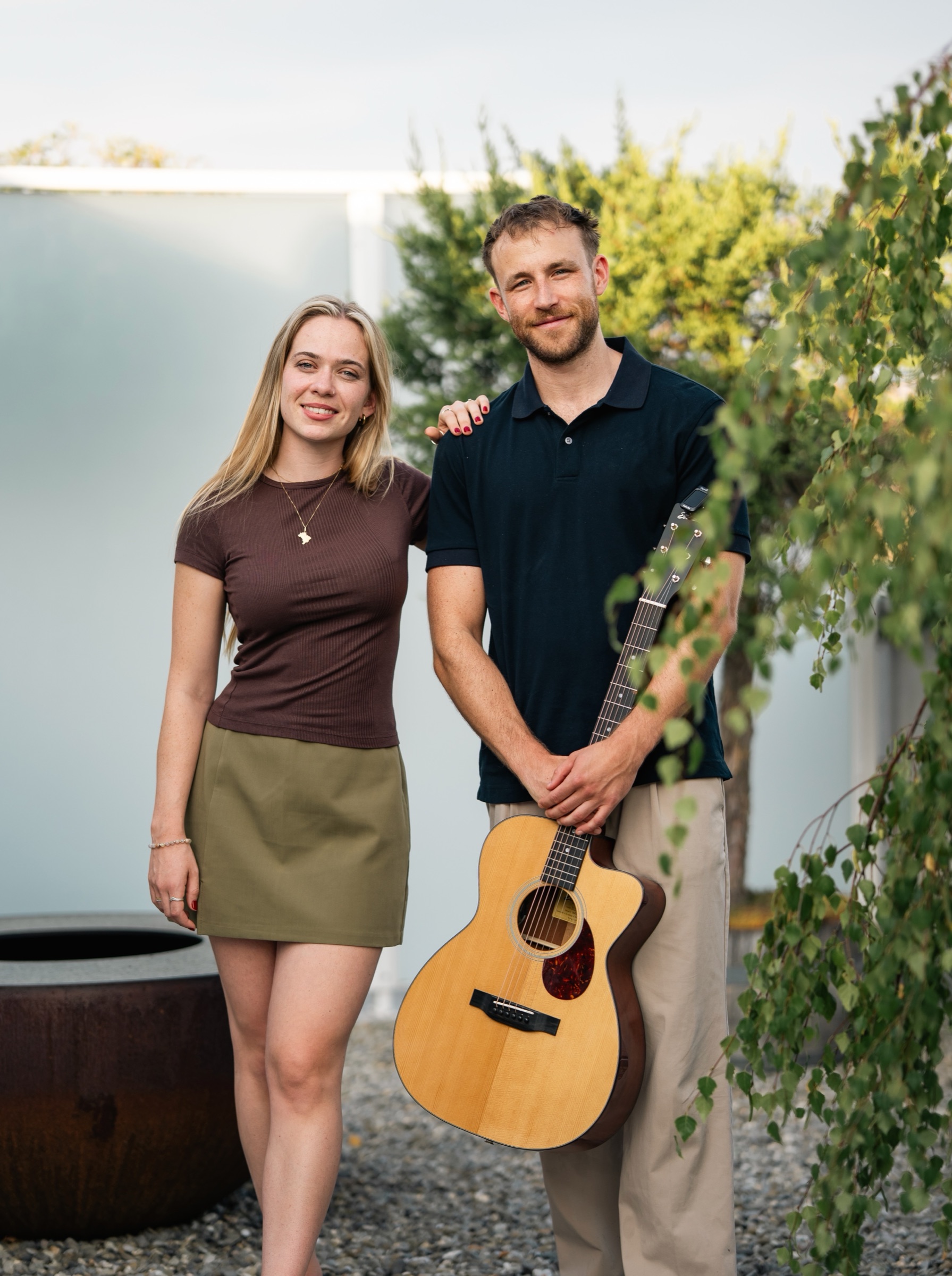 Helena und Elias lächeln gemeinsam im Freien, Elias hält eine Akustikgitarre